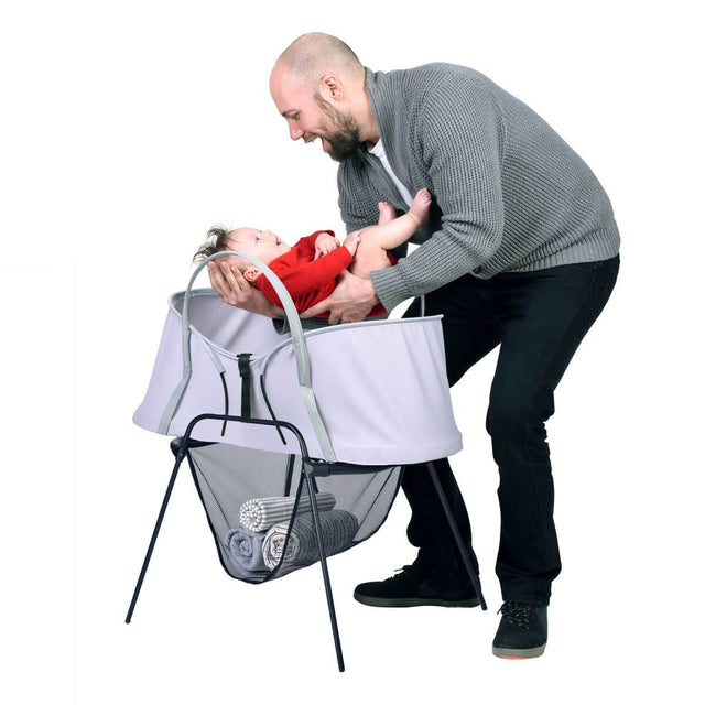 phil&teds carrycot stand with storage basket and nest baby bassinet on top and father taking baby out of bassinet 3/4 view_black